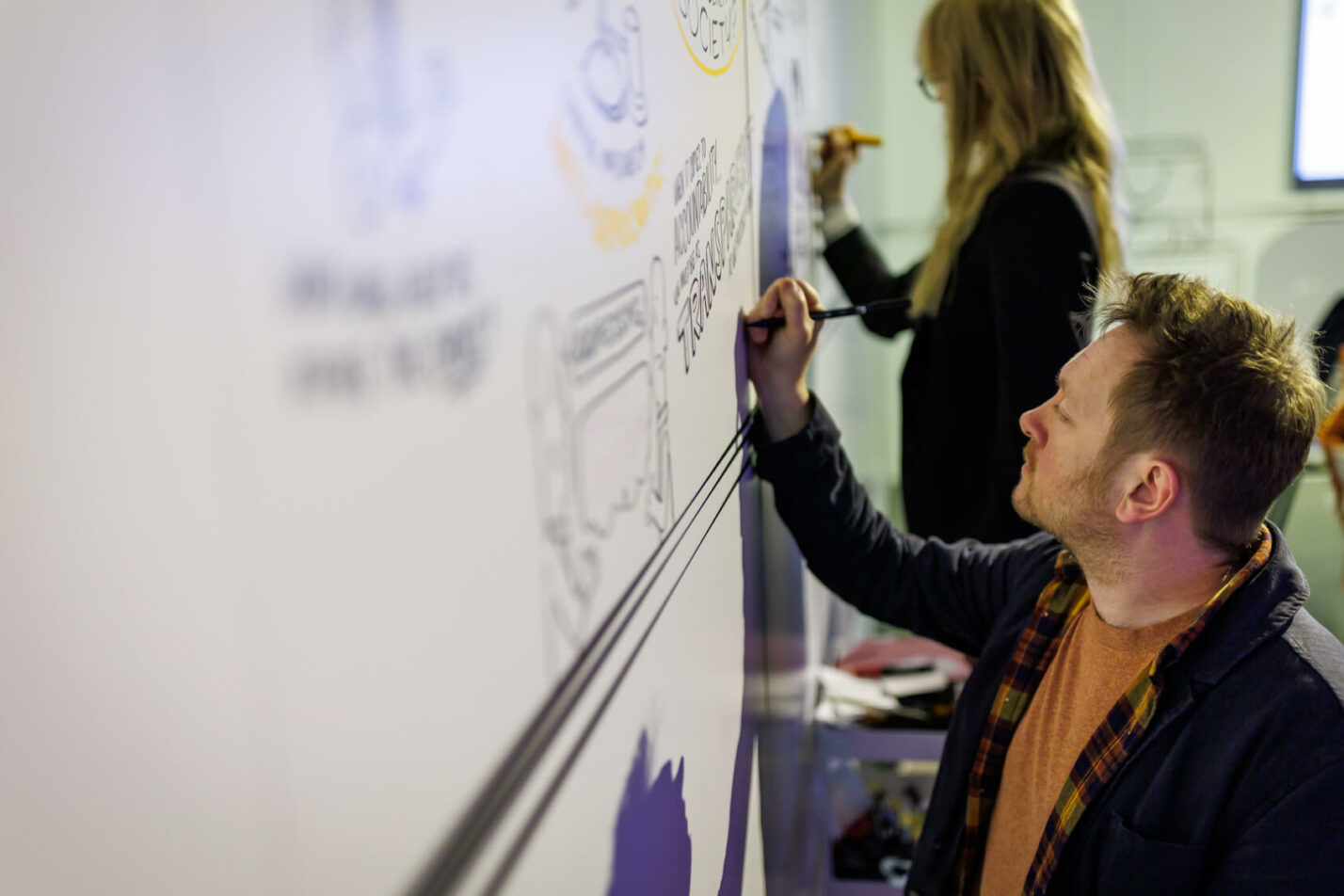 Graphic recorders illustrating ideas on a large wall during a strategy workshop, capturing insights in real time.
