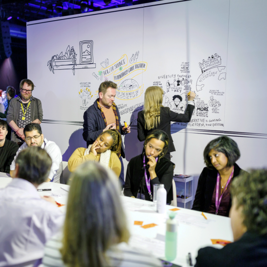 Two experienced live scribers from Smartup Visuals capturing key discussions in real-time at the Wellcome Trust event. Attendees are engaged in conversation at a table while the illustrators transform their insights into dynamic visuals on large Swedboard panels.